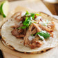 Carnitas on a grilled corn tortilla topped with cilantro and onion