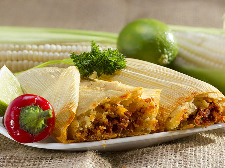 Plate of red pork tamales garnished with corn, lime, parsley, and red pepper