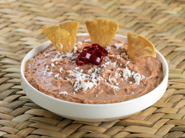 Refried beans in a white bowl garnished with chips and queso fresco